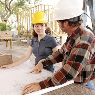 Two architects wearing hard hats discuss a design at a construction site