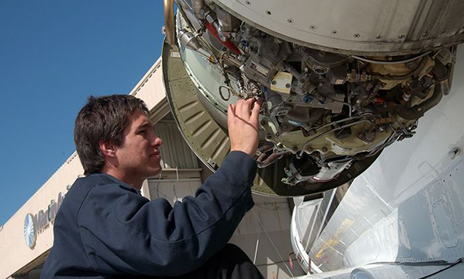 Aviation maintenance worker in blue jumpsuit works on engine of plane