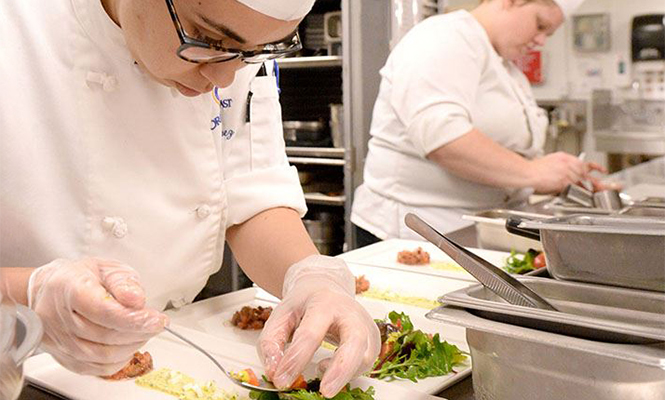 Culinary worker places garnishes on top of plates of salad