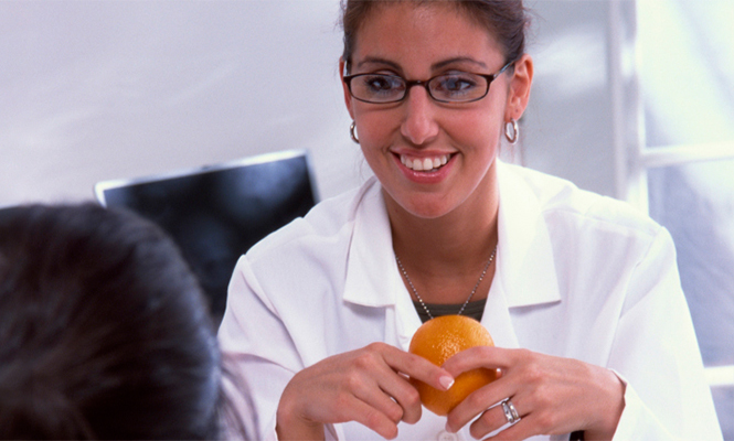 Nutritionist smiles at a patient while holding an orange, with more fruit on the table