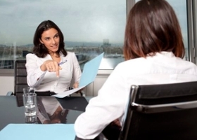 Woman in professional attire holds a folder and talks with another woman during a business meeting