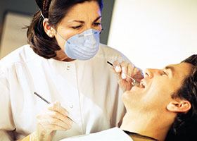 Female dental assistant uses tools to examine male patient's mouth