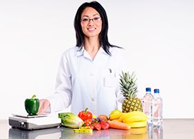 A nutritionist standing behind a table with fruits and vegetables