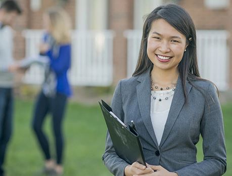 Real estate sales woman holding a folder smiles at camera with a couple in background