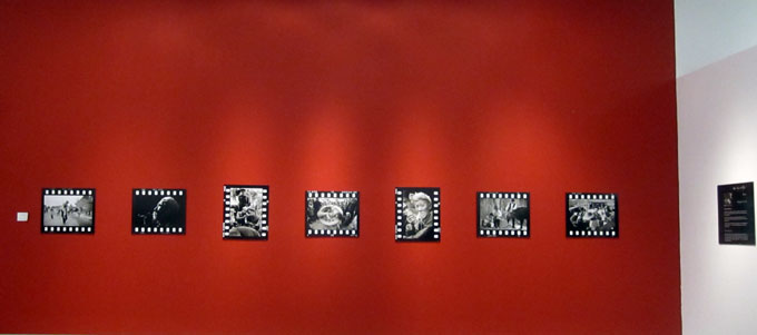 A row of photos hung on a red wall of the gallery