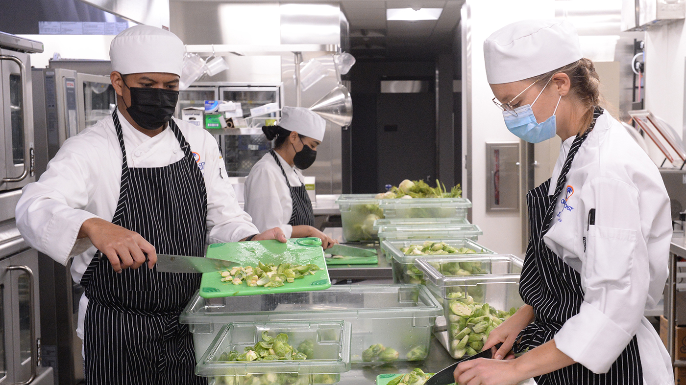 photo of two student chefs preparing food in industrial kitchen