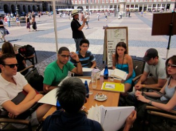 Group of students sitting talking at a table with plaza in background